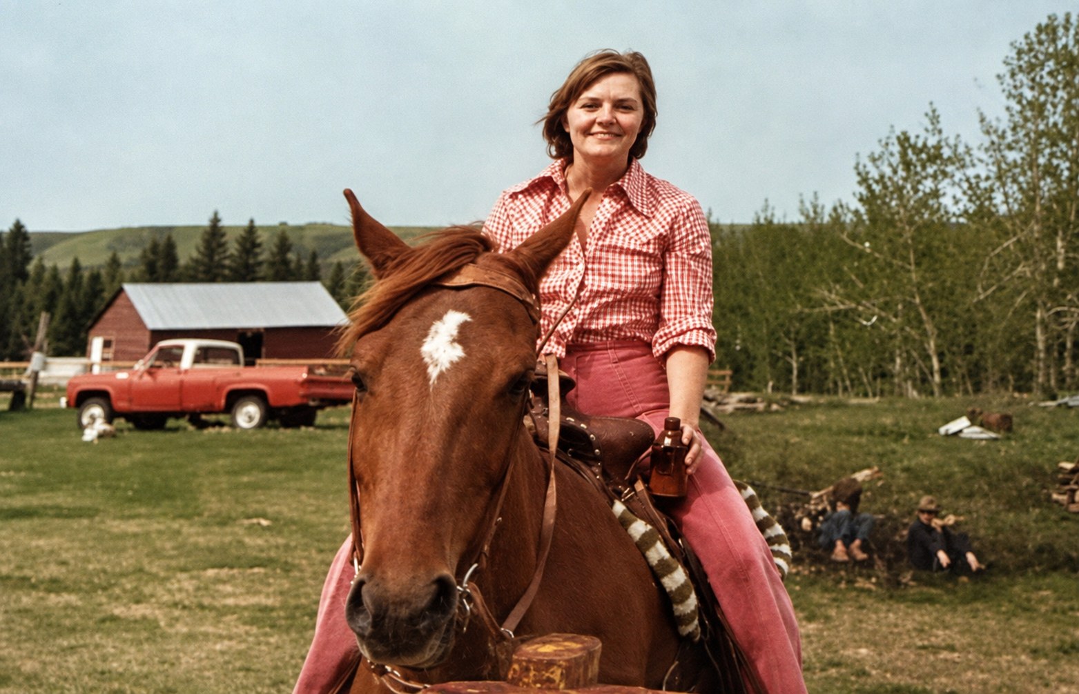 A younger Bette smiling while sitting on a brown horse at a farm with a red barn behind her